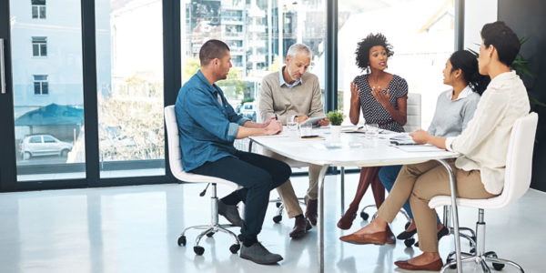 Shot of a group of coworkers talking together while sitting at a table in a meeting in an office